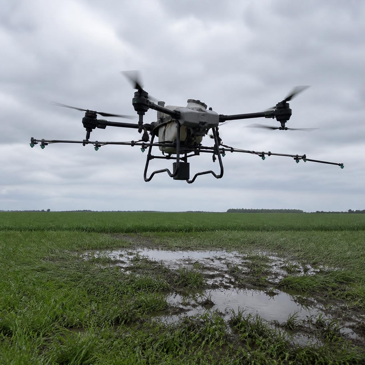 Agricultural spray drone hovering above a wet, rutted low spot in a green cereal crop